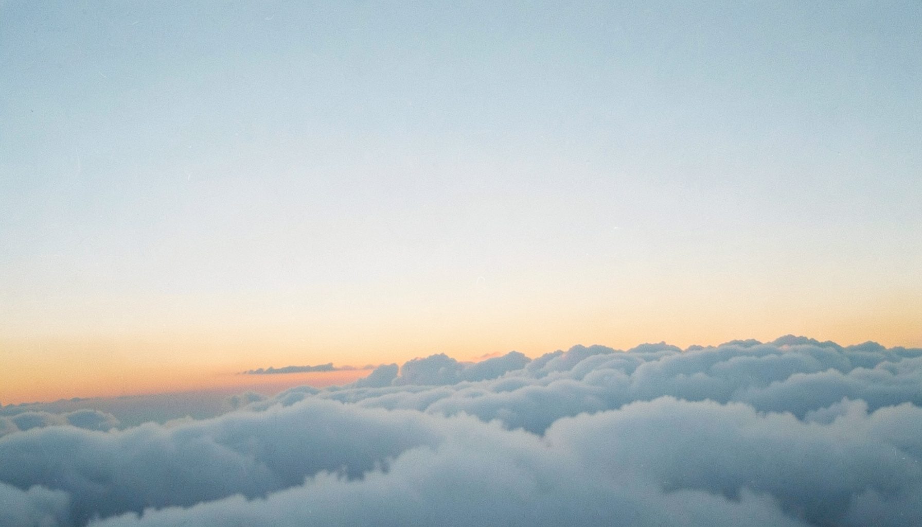 Soft gradient sky at dawn in pale blue and warm amber, suggesting a calm climb above the clouds