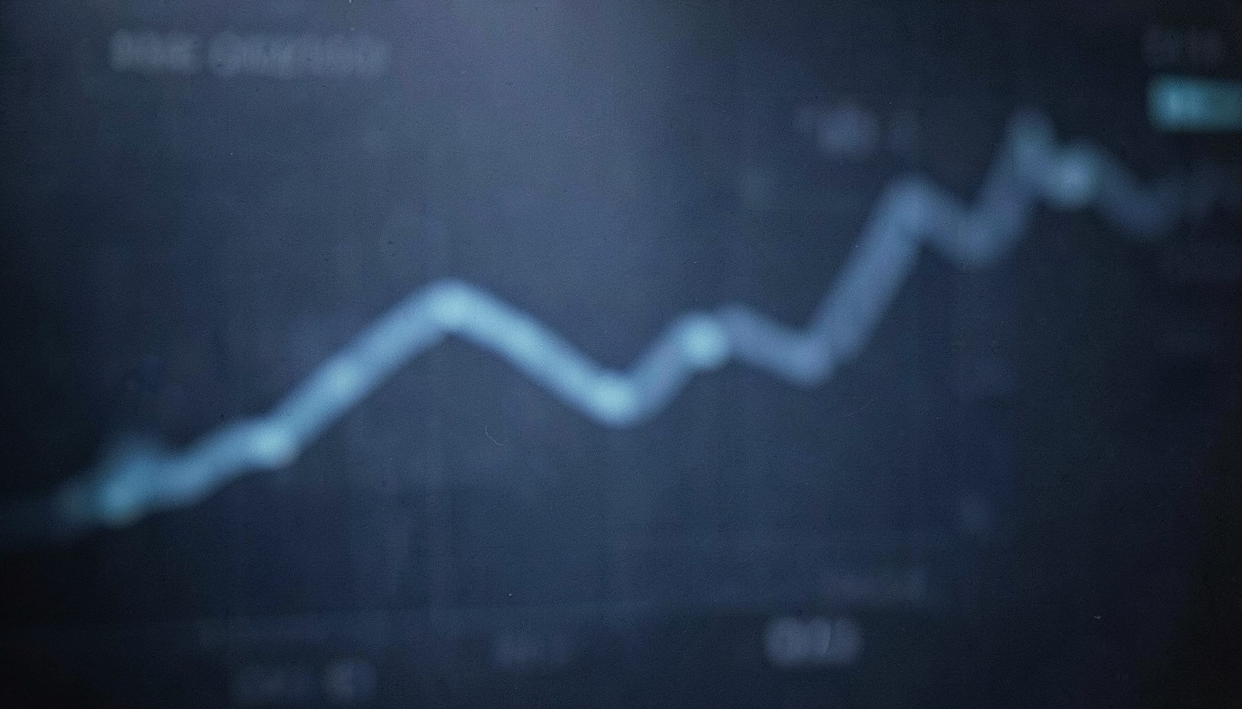 Soft-focus abstract dashboard with a rising graph line over a muted navy background, candid documentary style
